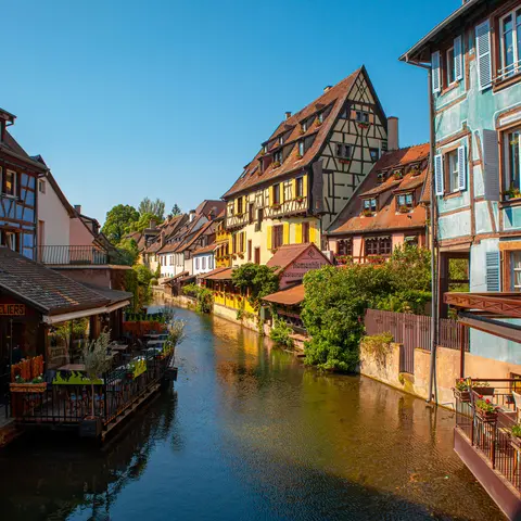 Maisons à colombages colorées bordant un canal, capturant le charme pittoresque d’un village alsacien sous le soleil.