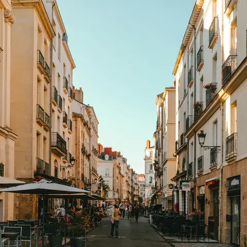 Rue animée avec immeubles haussmanniens, terrasses de cafés et passants profitant de l’ambiance chaleureuse en fin de journée