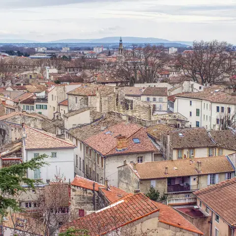 Vue sur les toits en tuiles d’une ville du sud de la France, avec ruelles et clochers, sous un ciel nuageux.