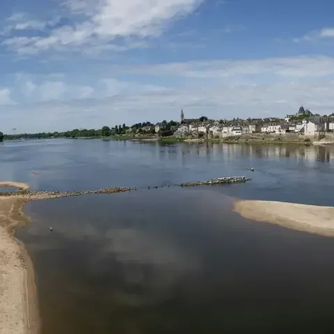 Rivière paisible avec bancs de sable sous un ciel bleu, offrant une vue sur un village pittoresque en bord de Loire.