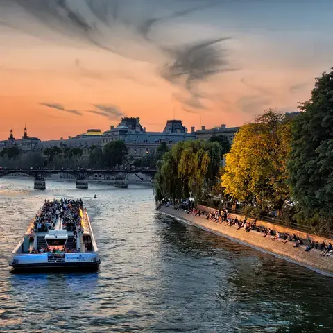Croisière sur la Seine au coucher du soleil, avec vue sur les quais animés et les monuments parisiens sous un ciel doré.