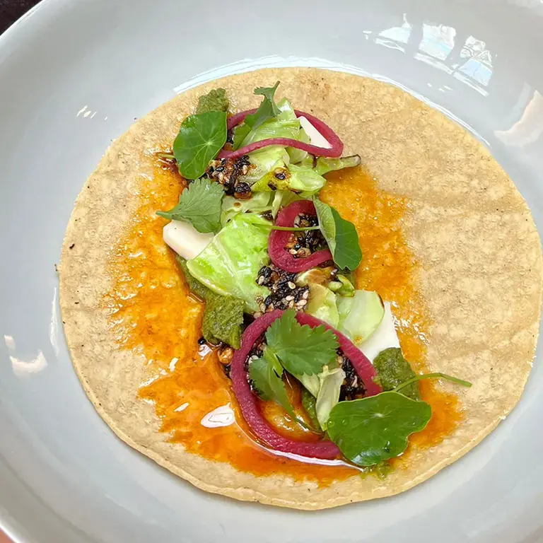 Tortilla de maïs avec des tiges de chou-fleur épicées et rôties, de la pâte de brocoli fermentée, de la salsa matcha et des c