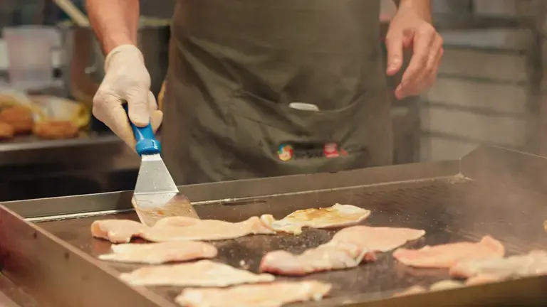 Chef grillant des blancs de poulet sur une plancha professionnelle