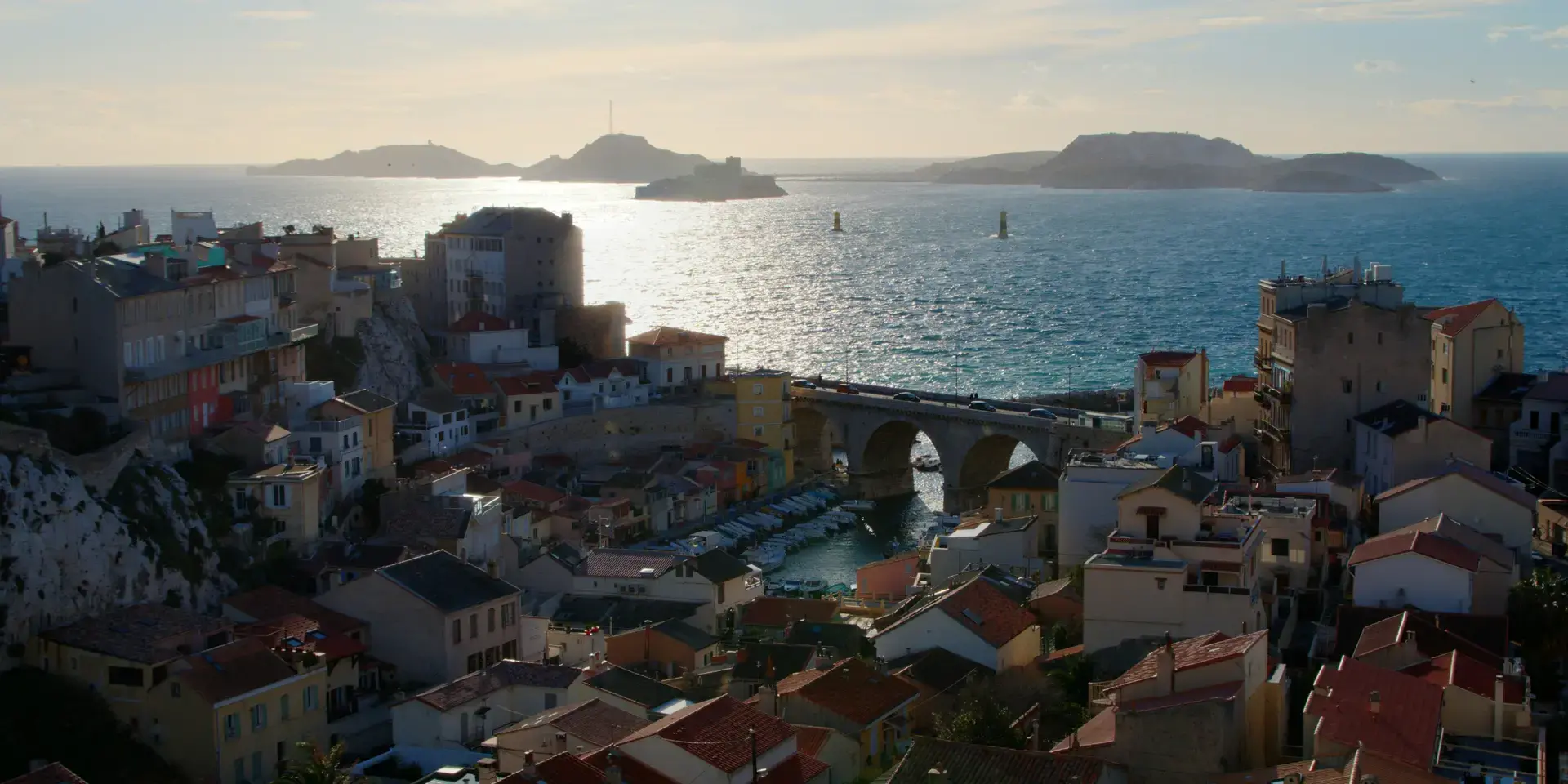 Vue sur le Vallon des Auffes à Marseille, port pittoresque aux maisons colorées, avec les îles du Frioul en arrière-plan.