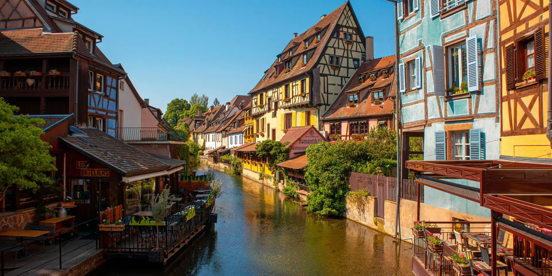 Maisons à colombages colorées bordant un canal, capturant le charme pittoresque d’un village alsacien sous le soleil.