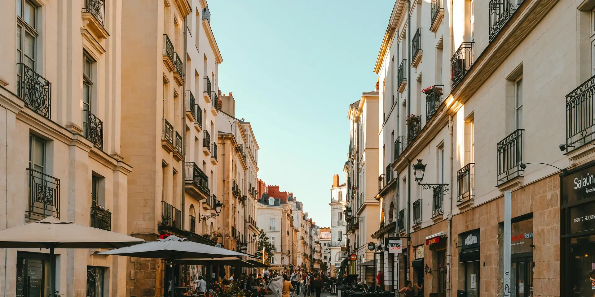Rue animée avec immeubles haussmanniens, terrasses de cafés et passants profitant de l’ambiance chaleureuse en fin de journée