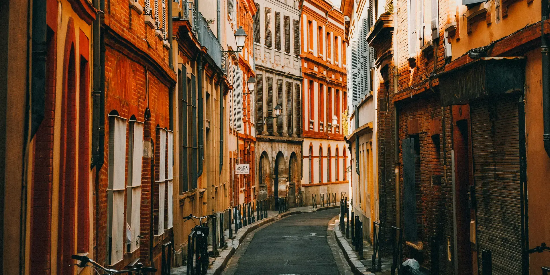 Ruelle pittoresque aux façades en briques rouges, baignée de lumière dorée, capturant l’âme authentique d’une ville du Sud.