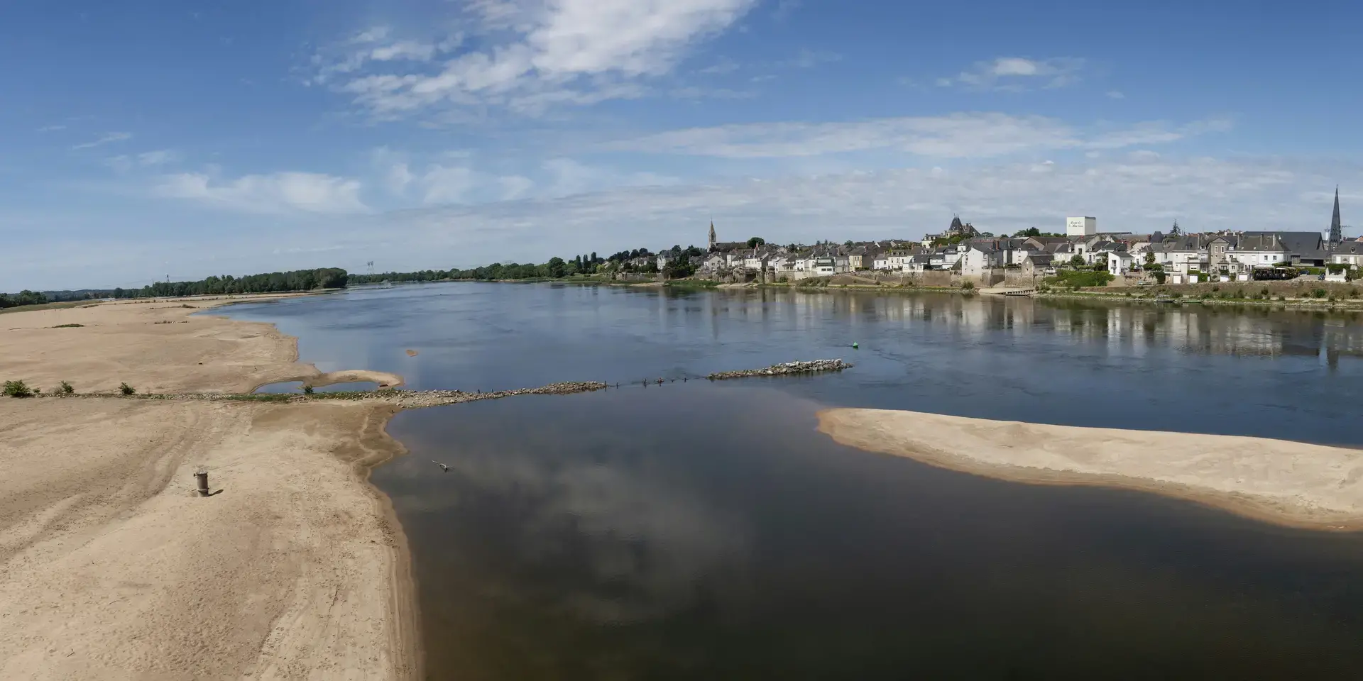 Rivière paisible avec bancs de sable sous un ciel bleu, offrant une vue sur un village pittoresque en bord de Loire.