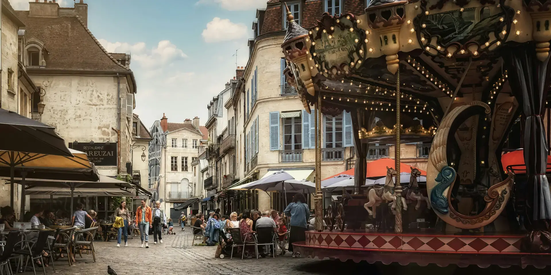 Place animée avec un carrousel rétro, terrasses de cafés et façades anciennes, capturant le charme d’une ville française.